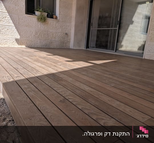 דק עץ מותקן בחצר בית עם קיר אבן